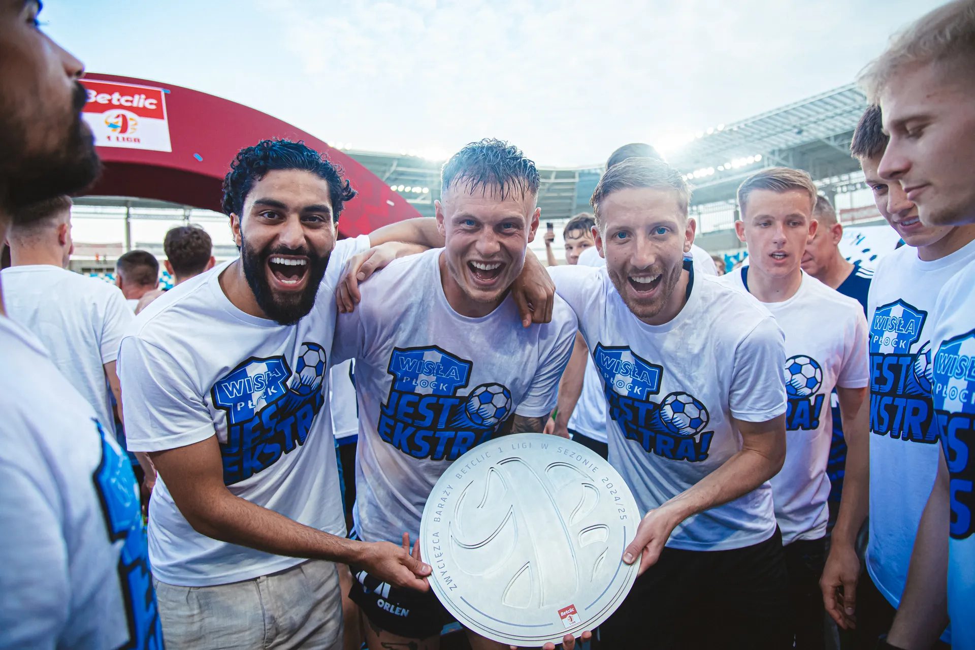 Uczestnicy wydarzenia sportowego radośnie trzymają puchar, ubrani w biało-niebieskie koszulki z napisem