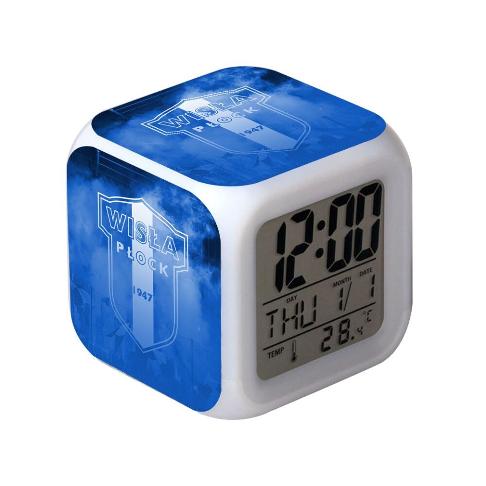 Budzik cyfrowy o sześciennym kształcie z białą obudową i niebieskimi bokami z logo Wisła Płock; na wyświetlaczu widnieje godzina 12:00, dzień i data oraz temperatura 28,4°C.