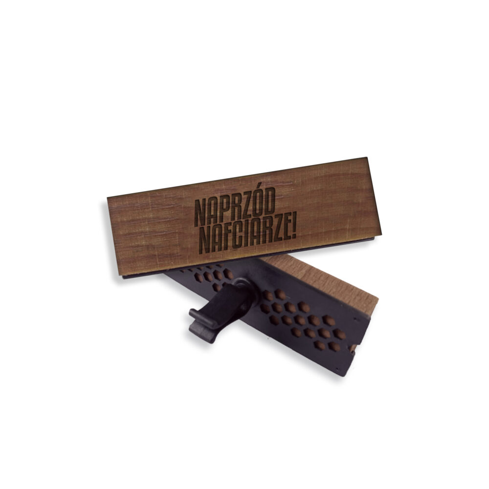 Drewniana tabliczka z napisem zamocowana na czarnym, perforowanym mechanizmie, sugerująca zapach drewniany.