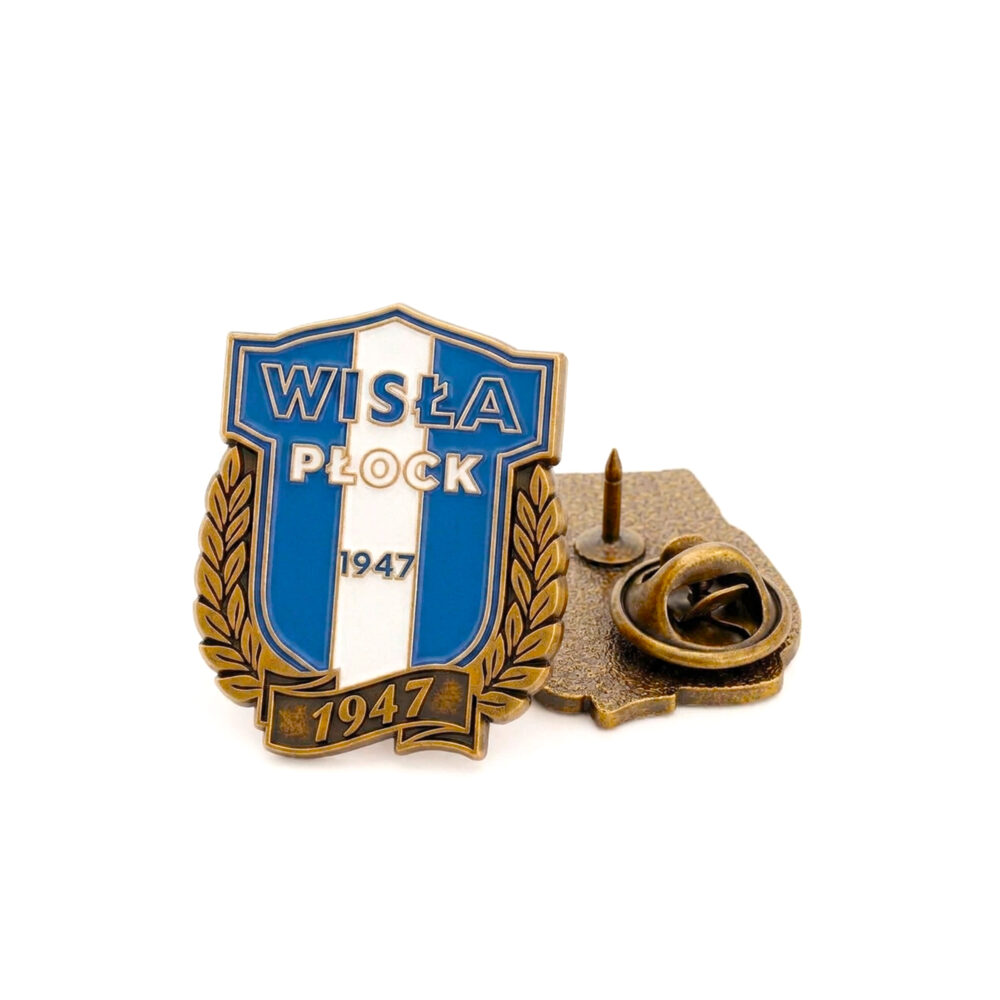 Emaliowany pin w kształcie herbu Wisły Płock: niebieska tarcza z białą pionową wstęgą, otoczona złotymi gałęziami laurowymi i napisem „Wisła Płock” oraz rokiem 1947, z tylnym zapięciem.