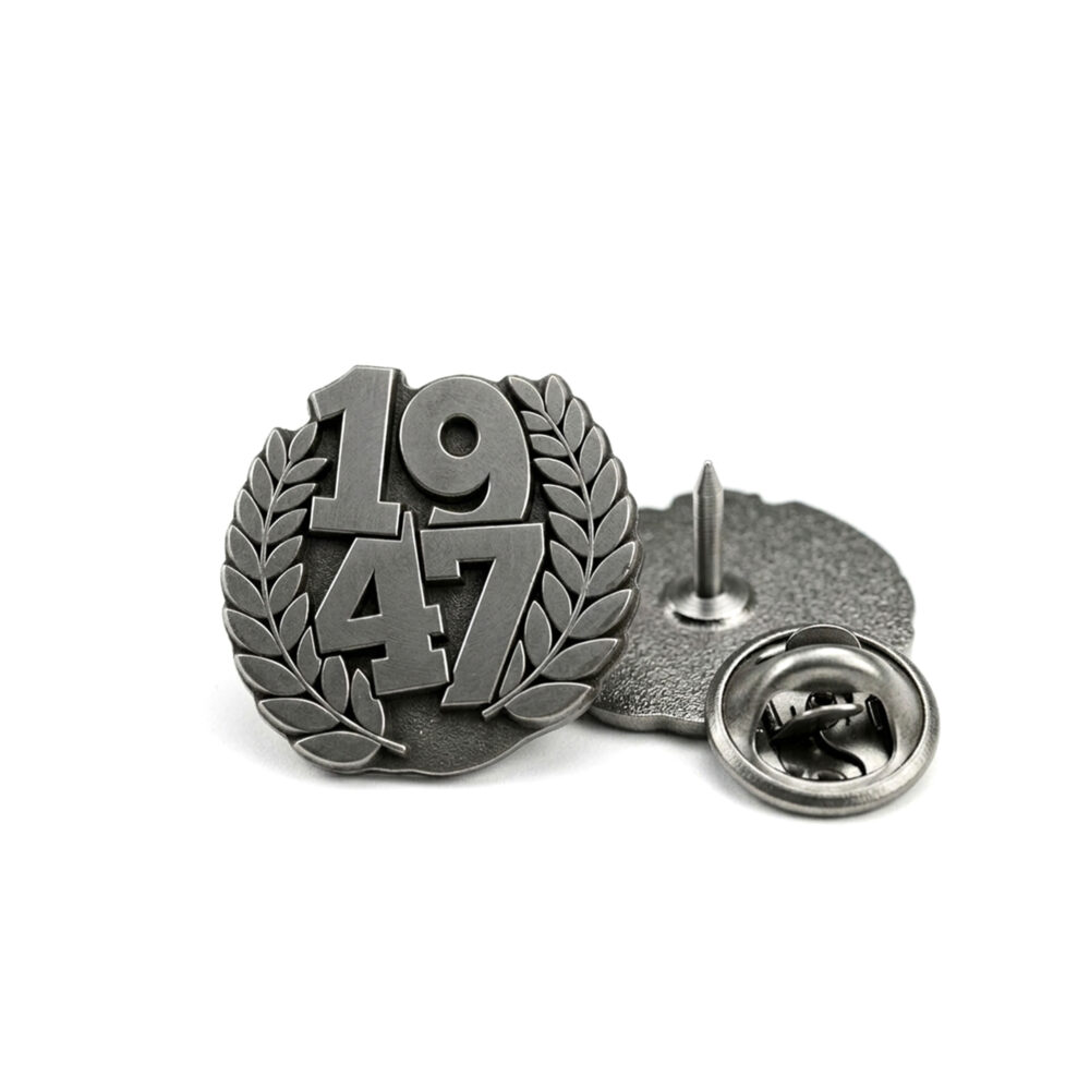 Metalowy pin do szalika z numerem 1947 otoczonym wieńcem laurowym.
