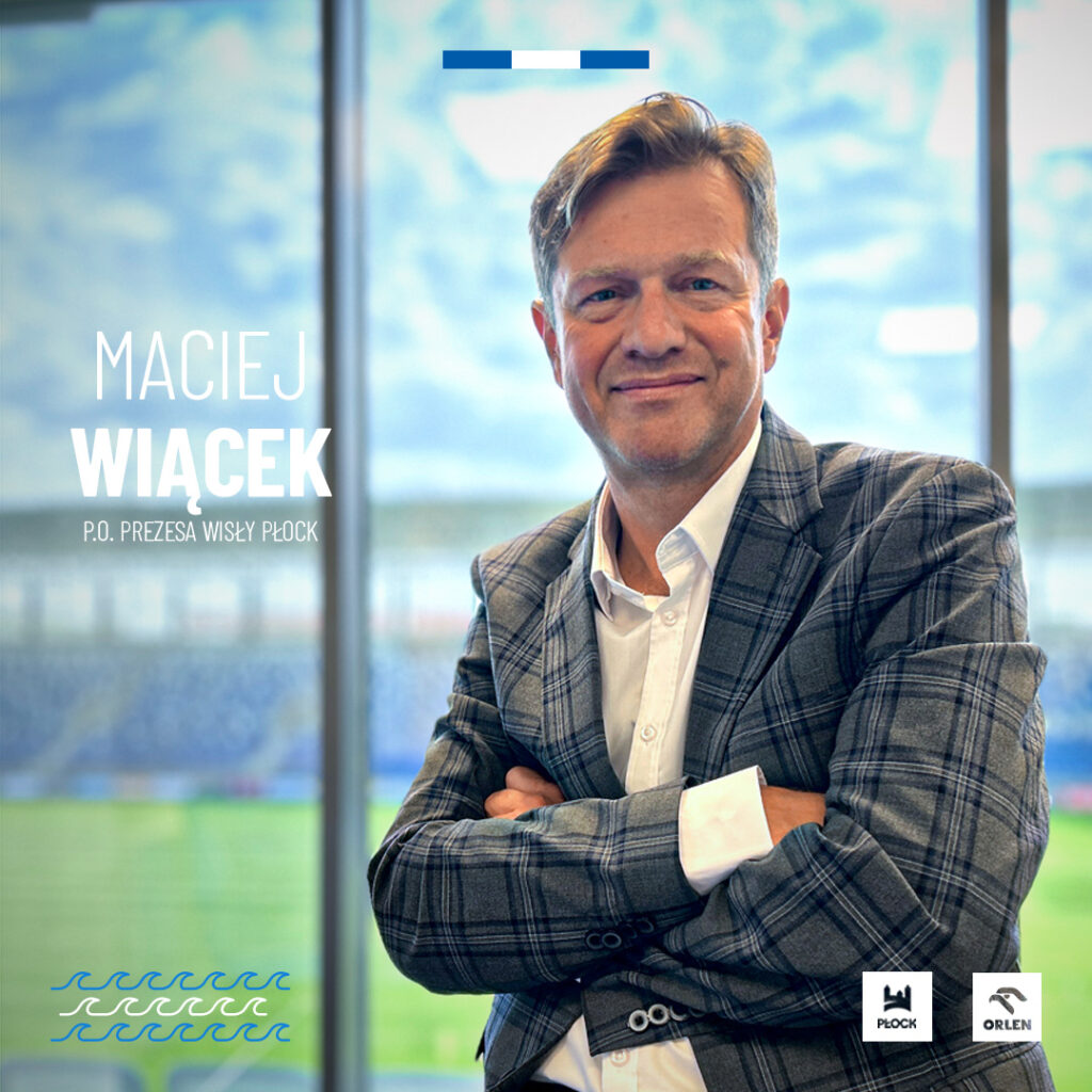 Maciej Wiącek, P.O. Prezes Wisły Płock, stoi z założonymi rękami na tle okien z widokiem na stadion.